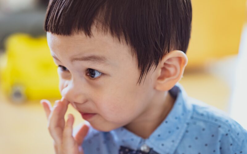 A young boy picking his nose.